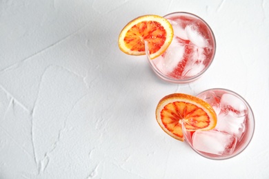 Glasses of drink with orange and ice cubes on white table, top view. Space for text