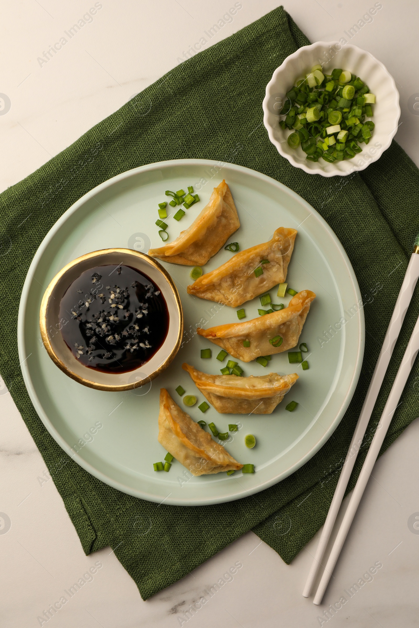 Photo of Delicious gyoza (asian dumplings) with soy sauce, green onions and chopsticks on white table, top view