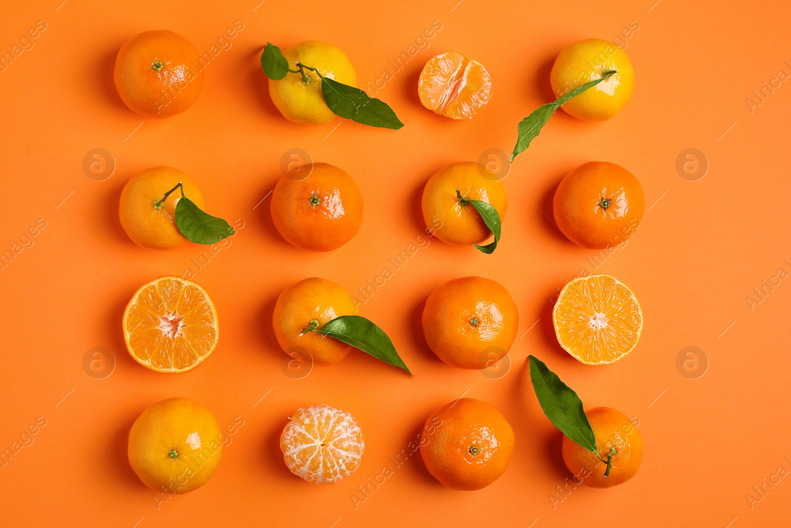 Photo of Delicious tangerines and green leaves on orange background, flat lay