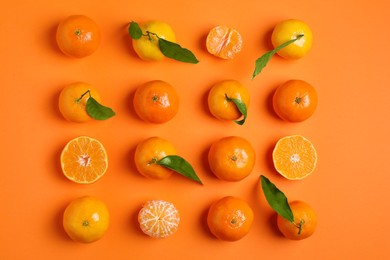 Delicious tangerines and green leaves on orange background, flat lay