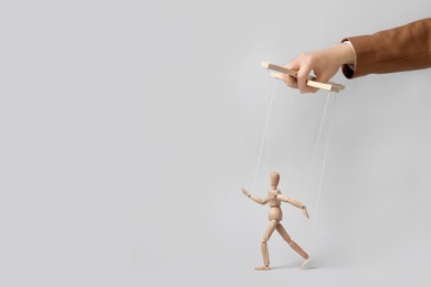 Woman pulling strings of puppet on light grey background, closeup. Space for text