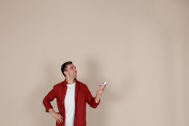 Young man operating air conditioner with remote control on light background