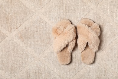 Photo of Fluffy beige slippers on soft carpet, top view. Space for text
