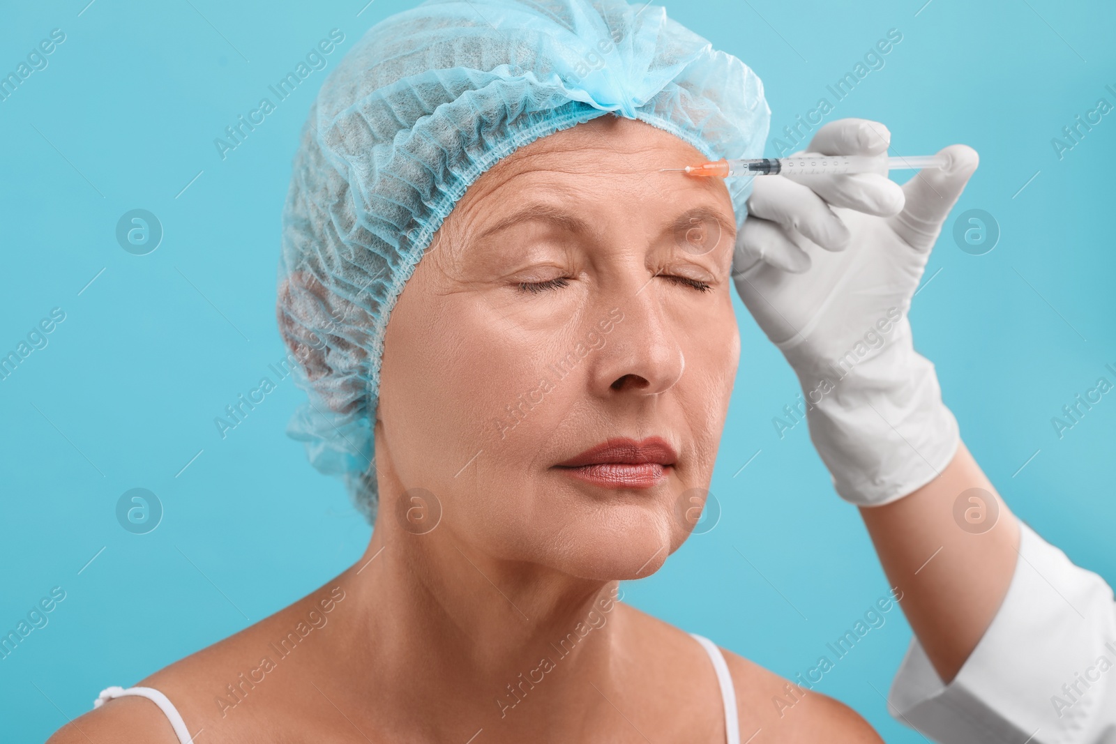 Photo of Doctor giving facial injection to senior woman on light blue background. Cosmetic surgery