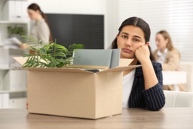 Unemployment problem. Woman with box of personal belongings at table in office