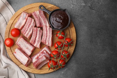 Photo of Cut raw pork ribs, tomatoes and sauce on grey table, top view. Space for text