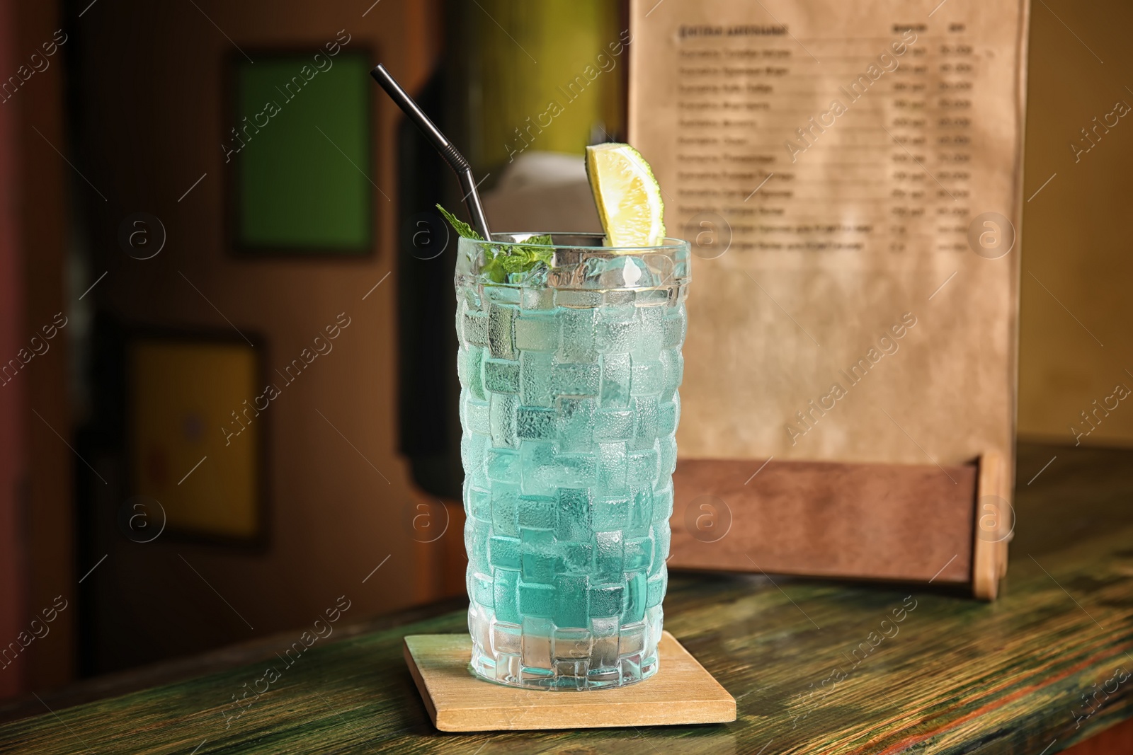 Photo of Glass with delicious cocktail and ice cubes on counter in bar