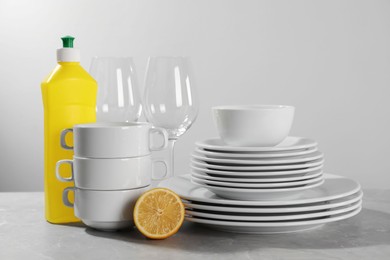 Photo of Clean tableware, glasses, dish detergent and halflemon on grey table against light background