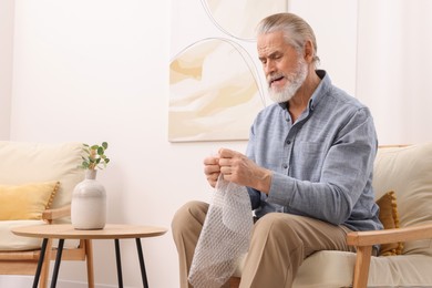 Photo of Emotional senior man popping bubble wrap at home. Stress relief