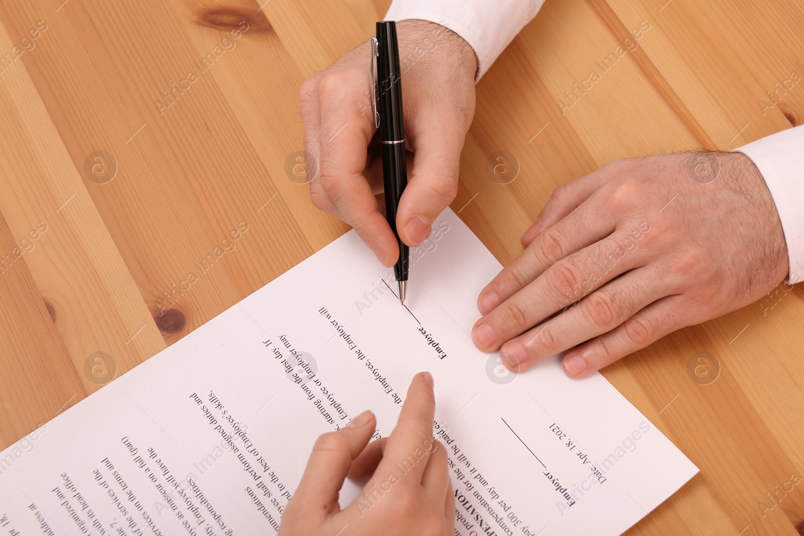 Photo of Businesspeople signing contract at wooden table, closeup of hands