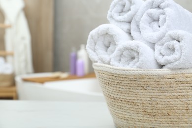 Photo of Wicker basket with rolled bath towels on white table in bathroom, closeup. Space for text