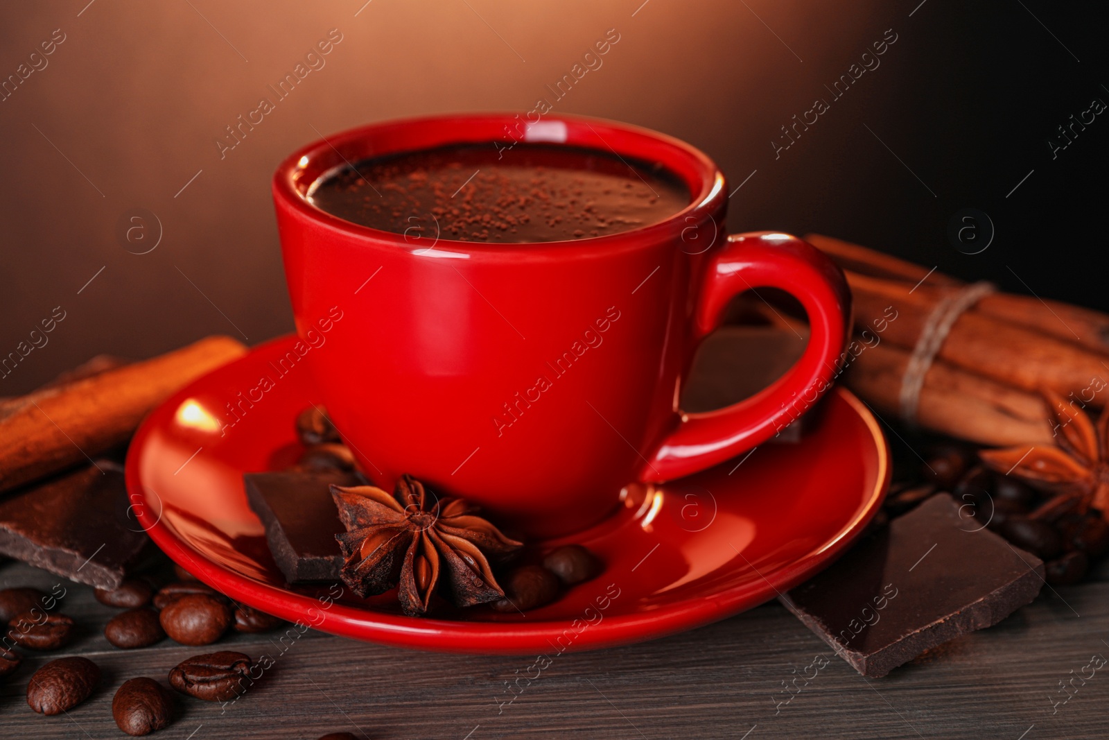 Photo of Cup of delicious hot chocolate, spices and coffee beans on wooden table