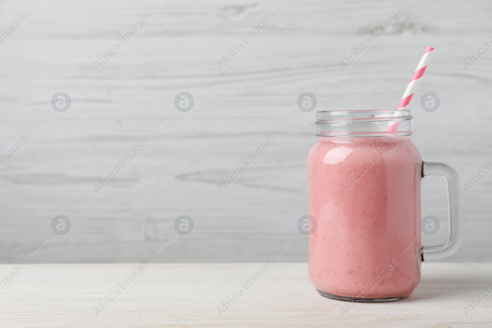 Photo of Mason jar with delicious berry smoothie on white wooden table. Space for text