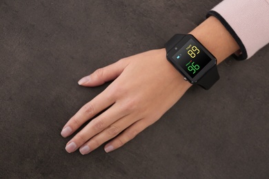 Image of Woman measuring oxygen level with smartwatch at grey table, top view