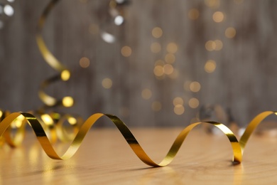 Photo of Shiny golden serpentine streamer on wooden table against blurred lights. Space for text