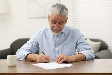 Senior man signing Last Will and Testament at wooden table indoors