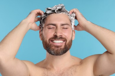Happy man washing his hair with shampoo on light blue background, closeup