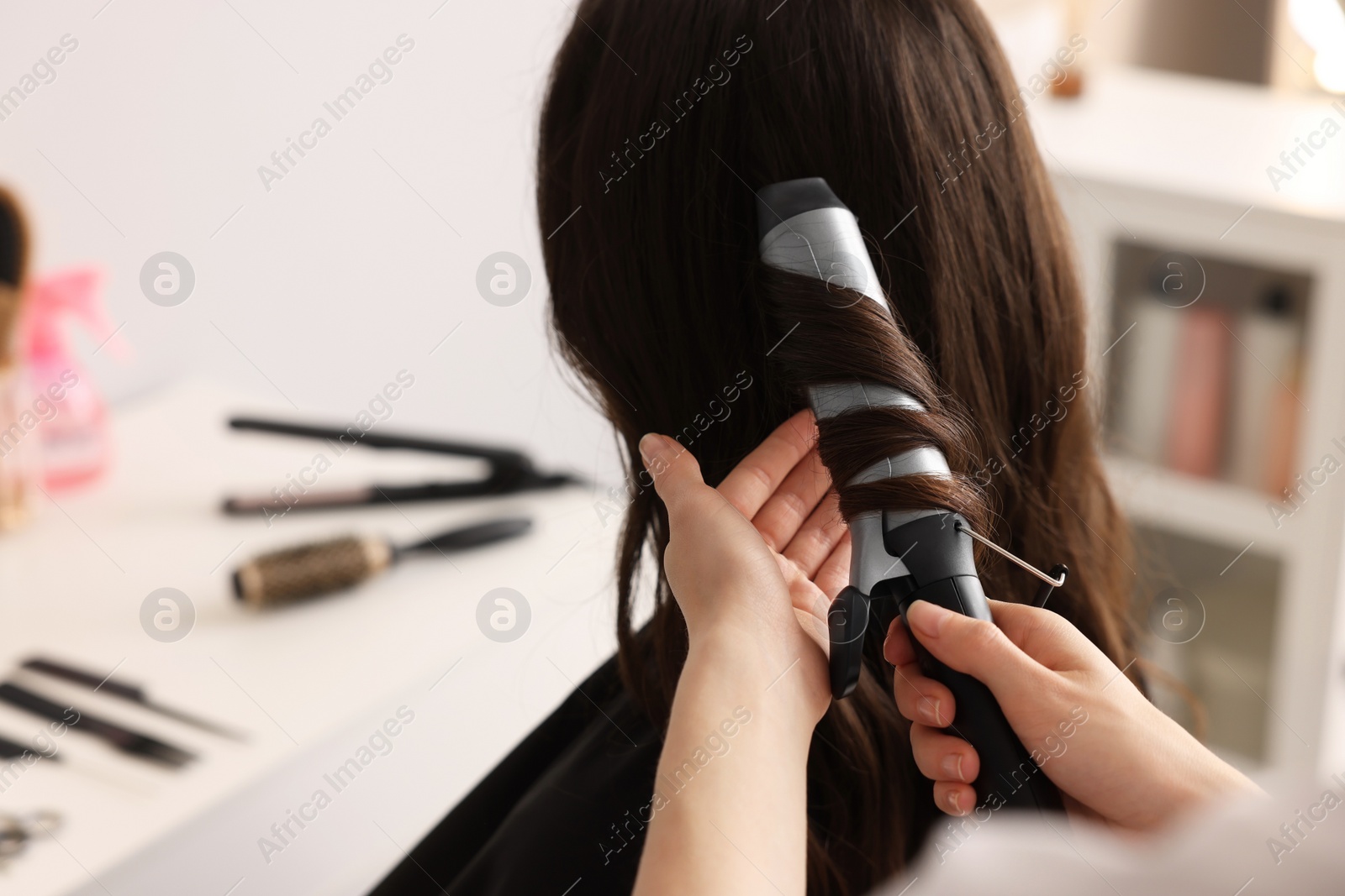 Photo of Hairdresser working with client using curling hair iron in salon, closeup