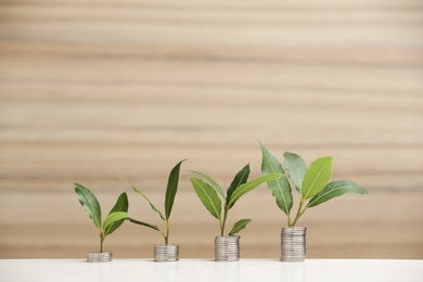 Photo of Stacked coins and green plants on white table against blurred background. Space for text