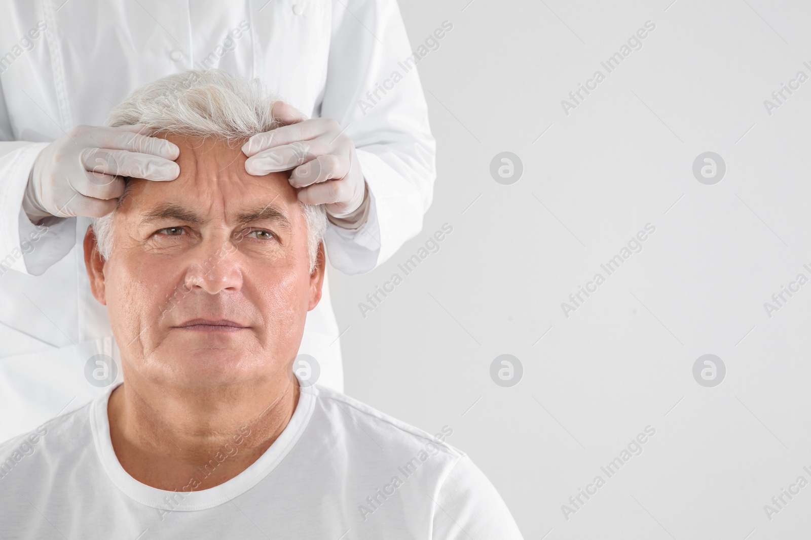 Photo of Doctor examining senior man face before cosmetic surgery on white background. Space for text