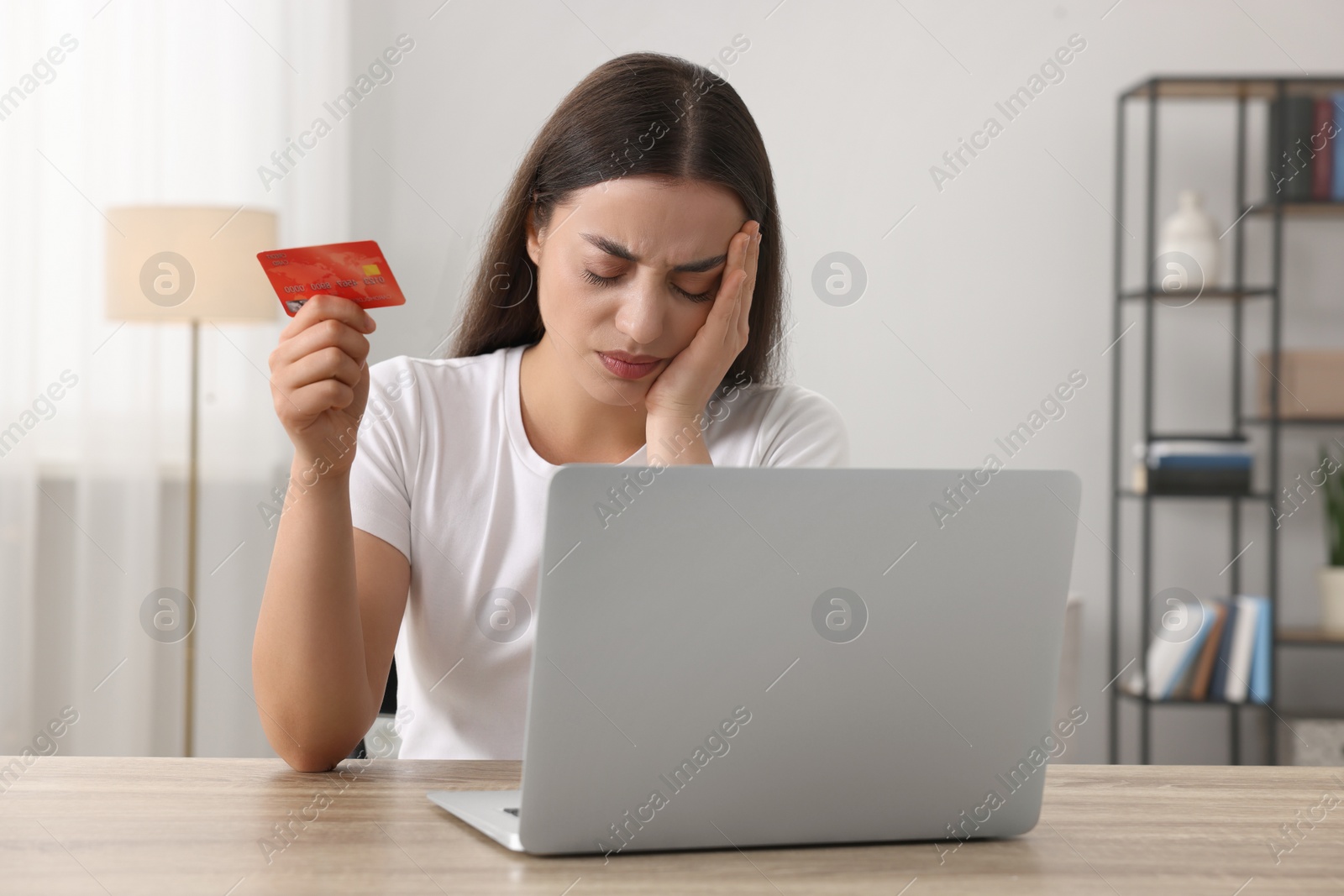 Photo of Stressed woman with credit card and laptop at table indoors. Be careful - fraud