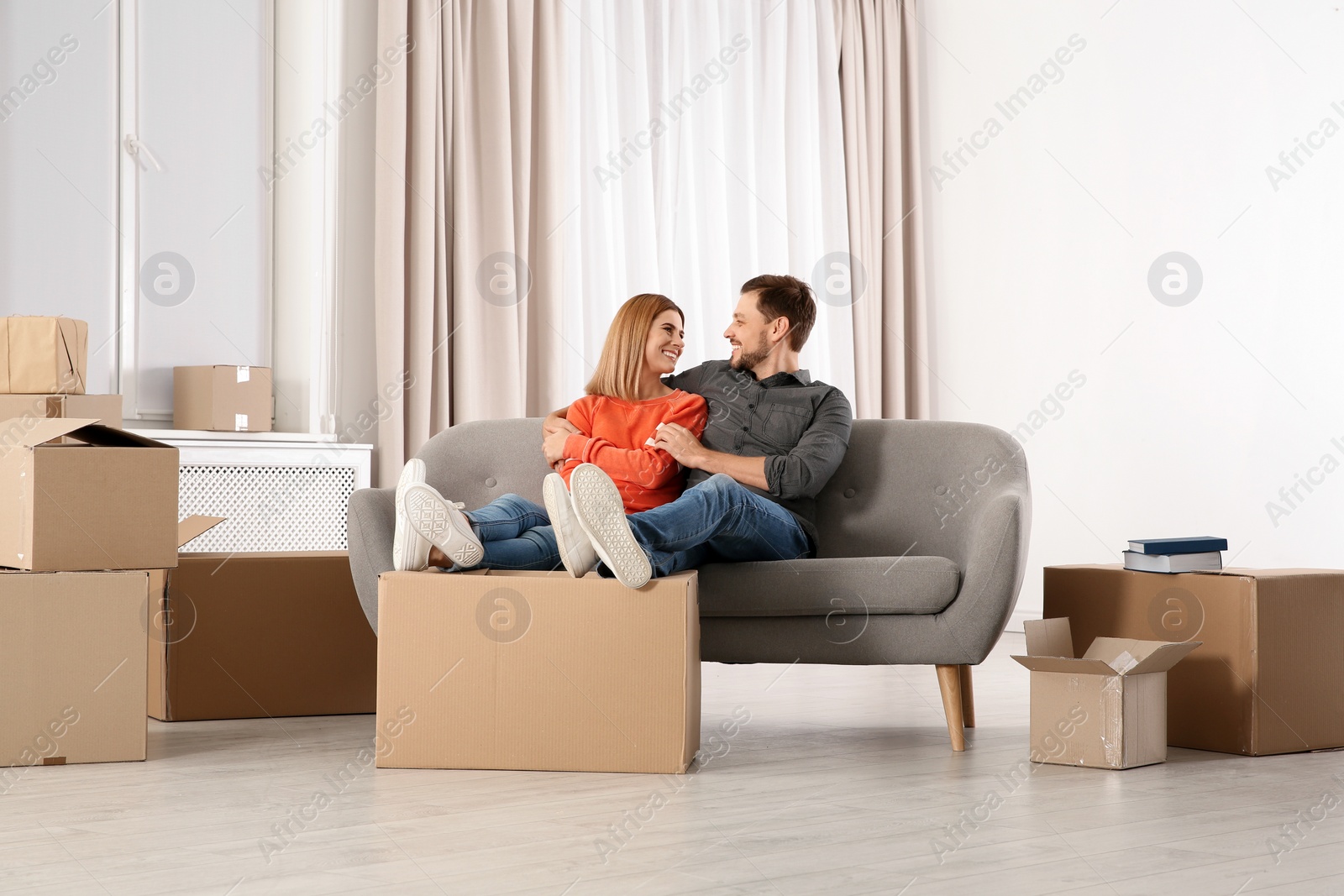 Photo of Couple resting on sofa near moving boxes in their new house