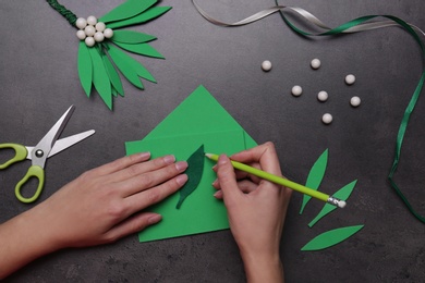 Woman making mistletoe branch on grey table, top view