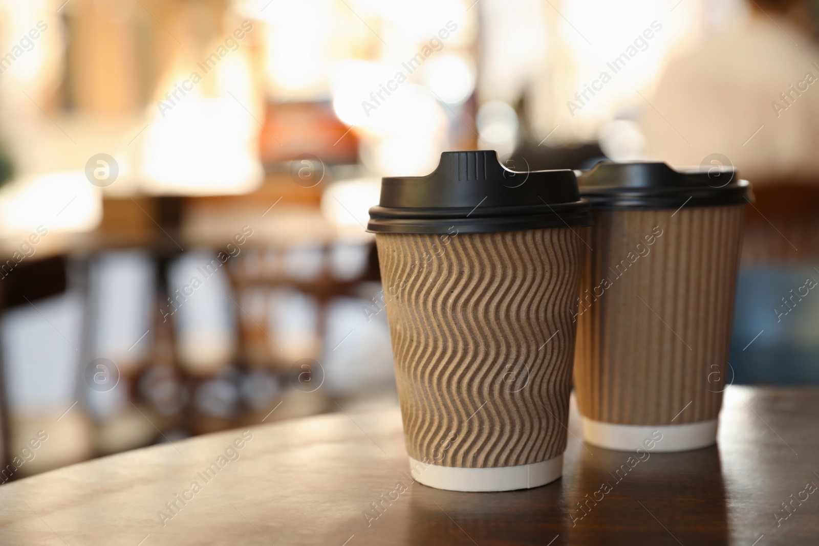 Photo of Cardboard takeaway coffee cups with plastic lids on wooden table in city, space for text