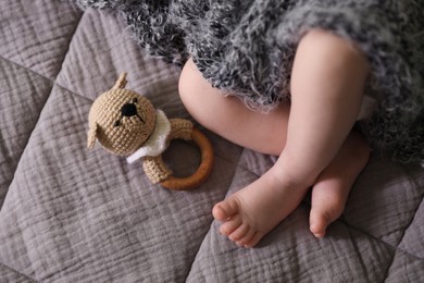 Photo of Adorable newborn baby with grey fluffy blanket and teething toy in bed, closeup