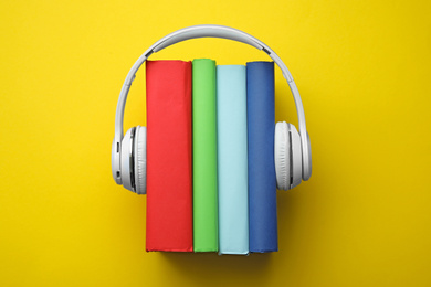 Photo of Books and modern headphones on yellow background, top view