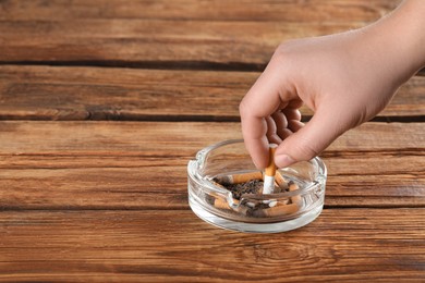 Photo of Man putting out cigarette in ashtray on wooden table, closeup. Space for text