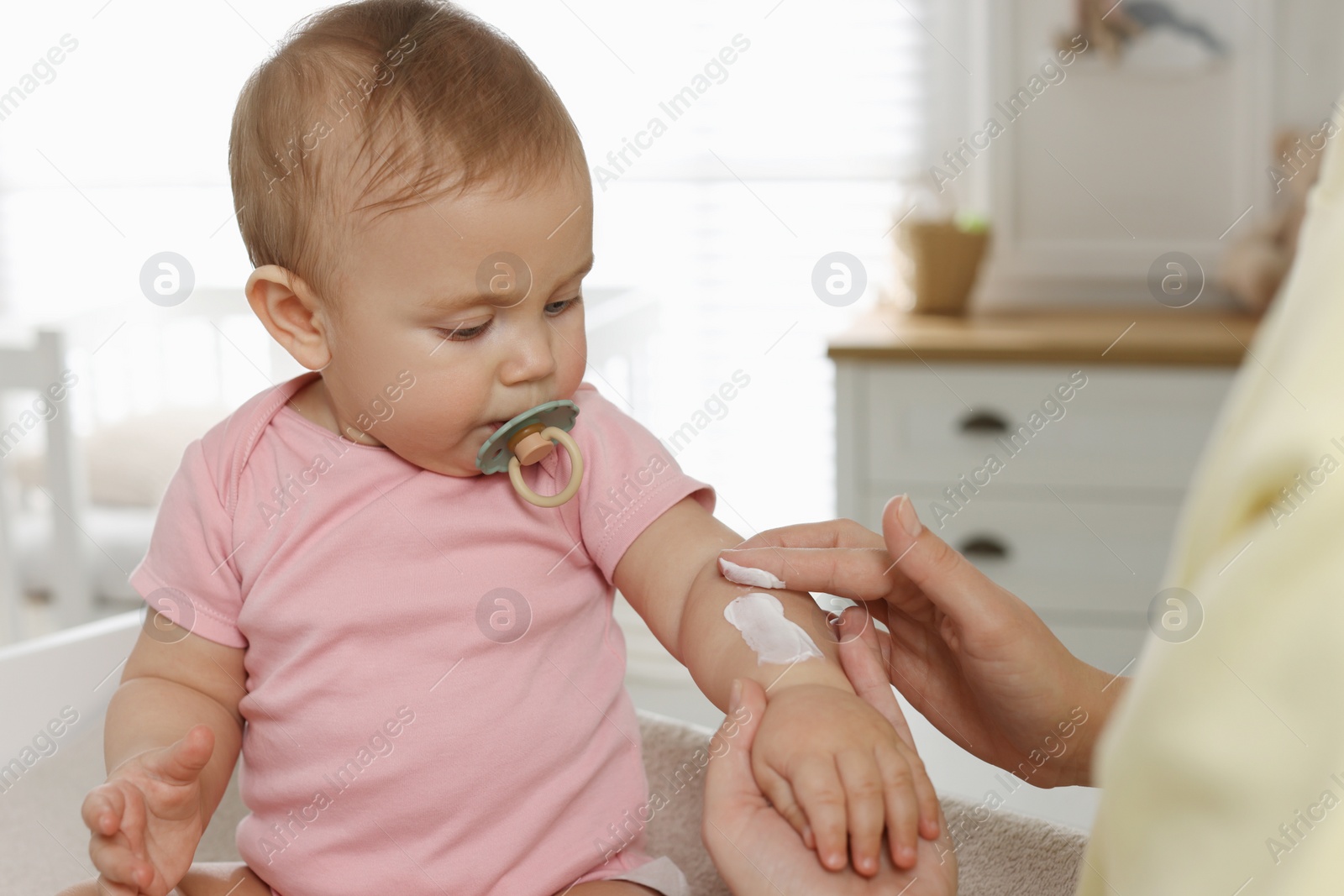 Photo of Mother applying body cream on her little baby at home, closeup