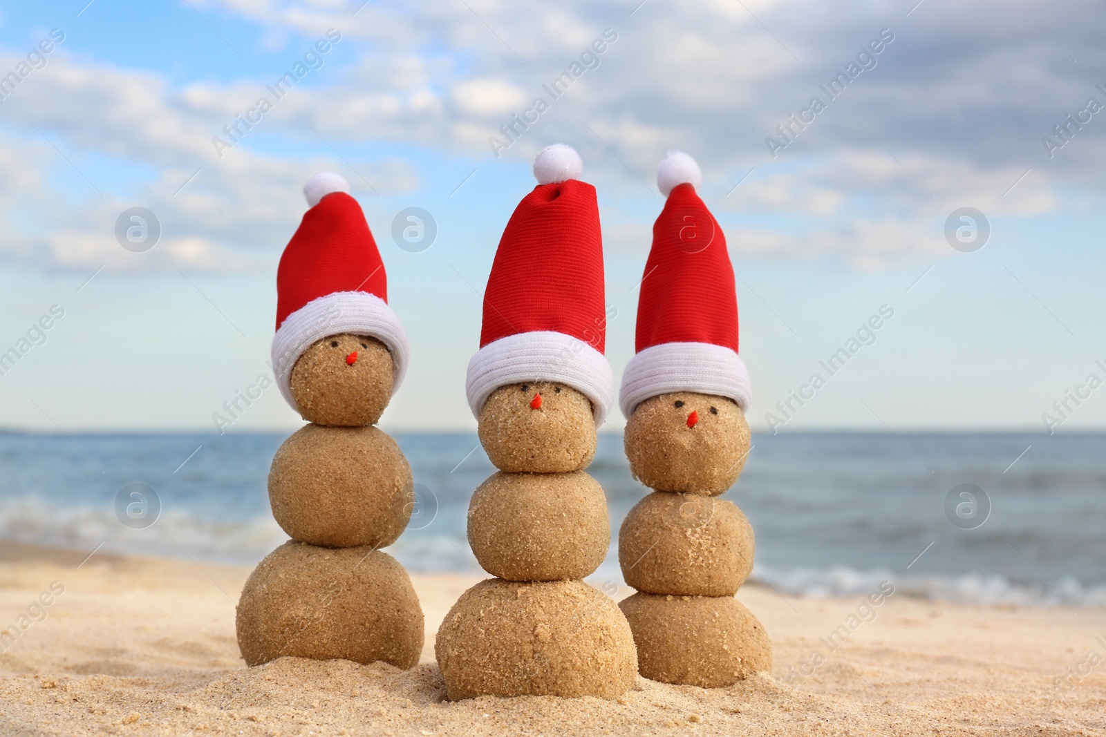 Photo of Snowmen made of sand with Santa hats on beach near sea. Christmas vacation