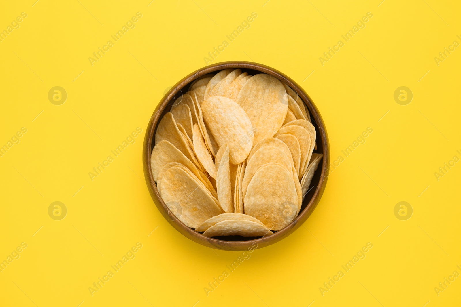 Photo of Bowl of tasty potato chips on yellow background, top view