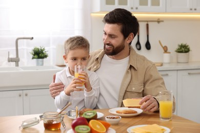 Photo of Father and his cute little son having breakfast at table in kitchen