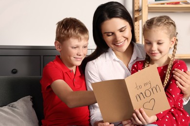 Photo of Happy woman receiving greeting card from her children at home