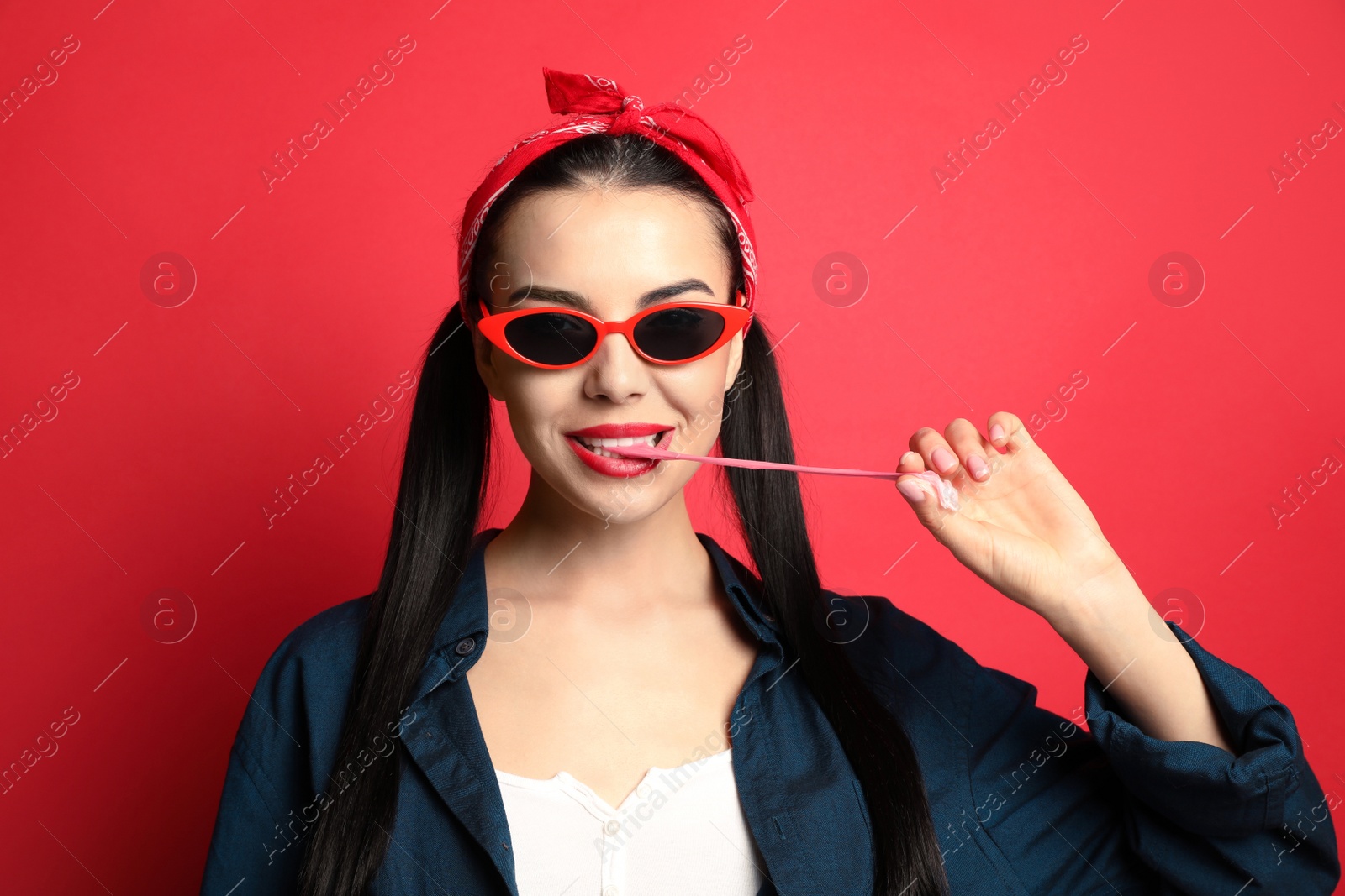 Photo of Fashionable young woman in pin up outfit chewing bubblegum on red background