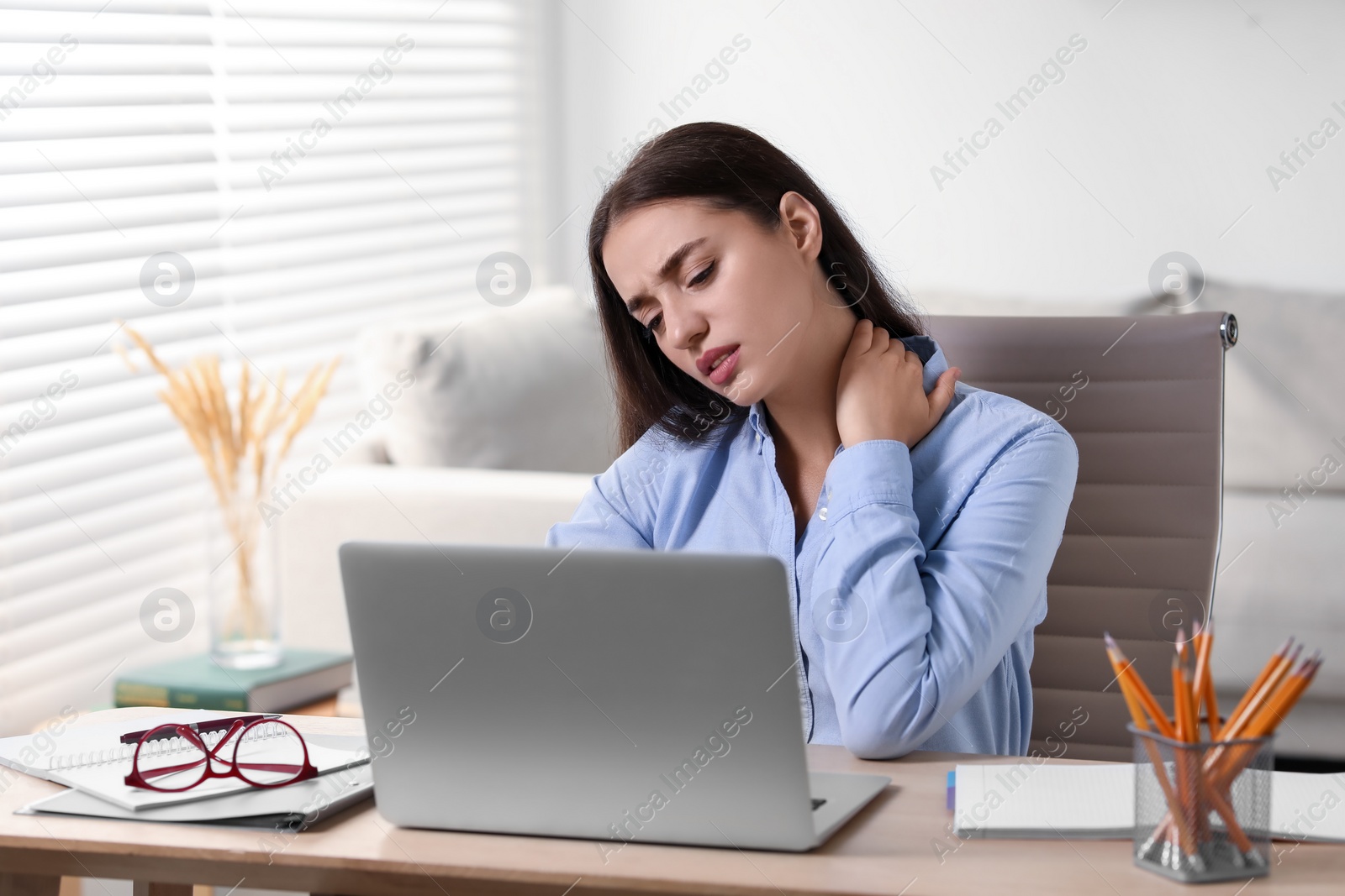 Photo of Young woman suffering from neck pain at table in office