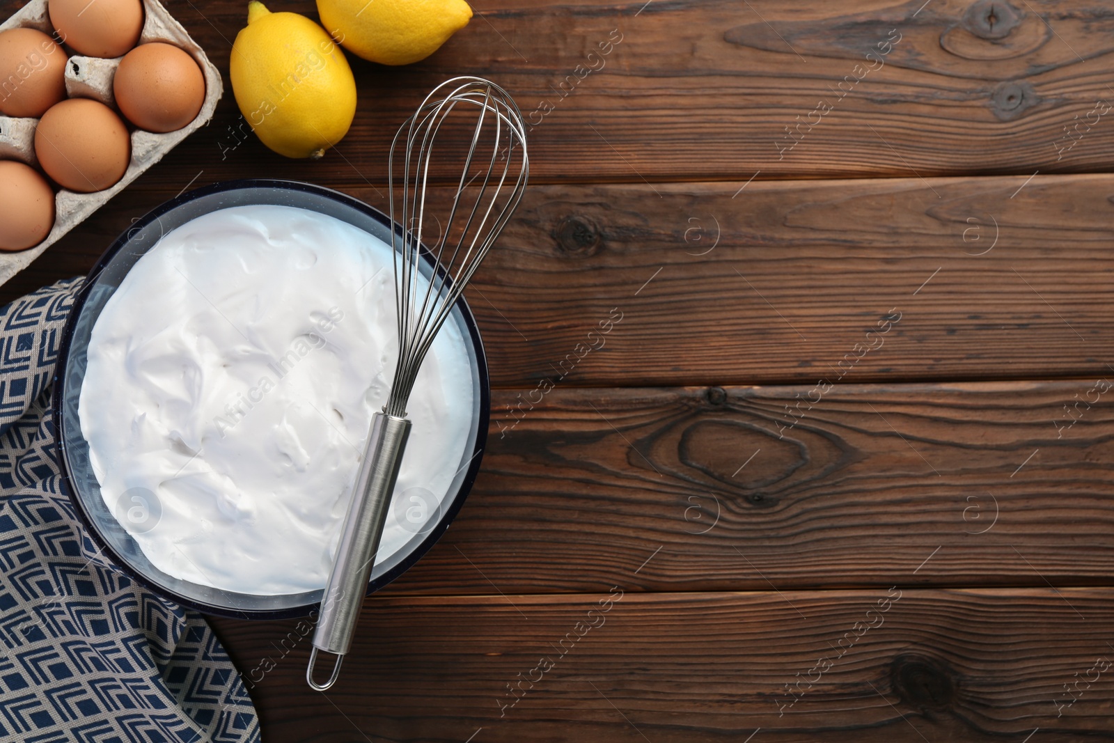 Photo of Bowl with whipped cream, whisk and ingredients on wooden table, flat lay. Space for text