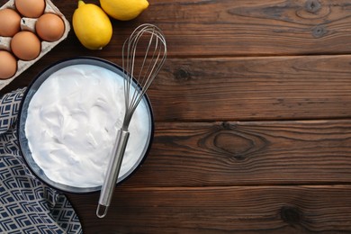 Photo of Bowl with whipped cream, whisk and ingredients on wooden table, flat lay. Space for text