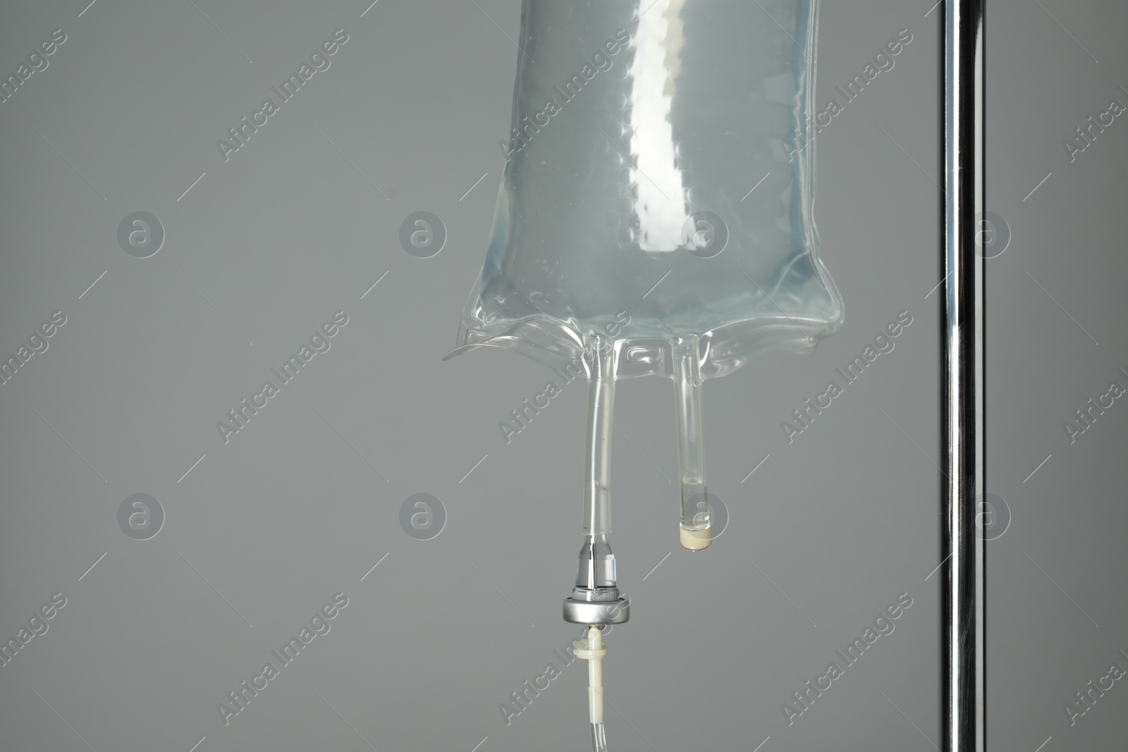 Photo of IV infusion set on pole against grey background, closeup. Space for text