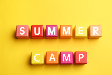 Photo of Colorful wooden cubes with phrase SUMMER CAMP on yellow background, flat lay