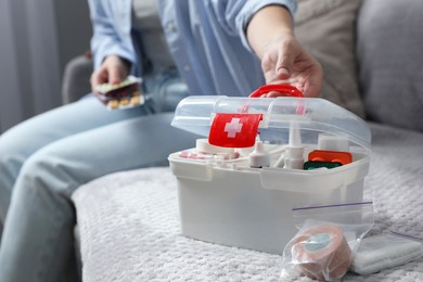 Photo of Woman holding pills indoors, focus on first aid kit