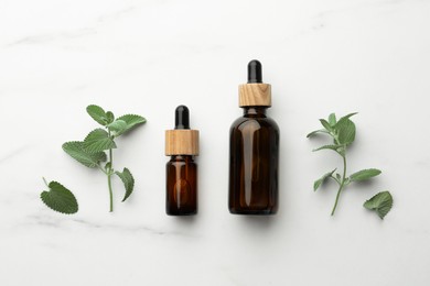 Bottles of mint essential oil and fresh herb on white marble table, flat lay