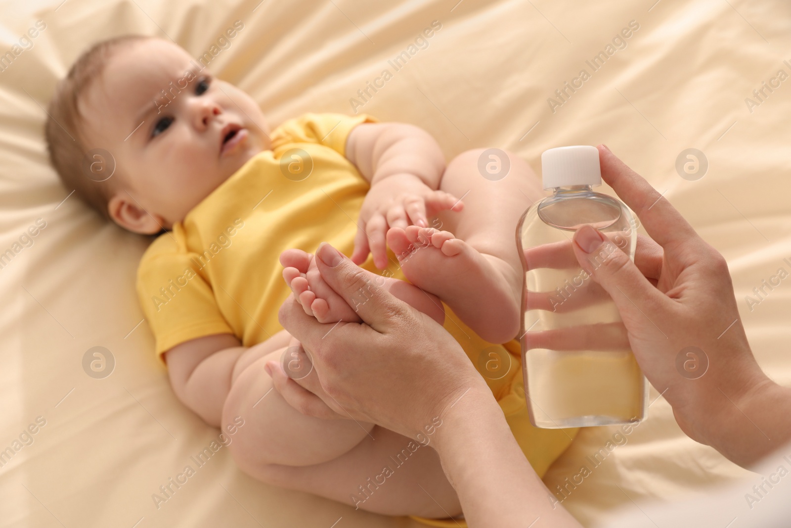 Photo of Mother massaging her cute baby with oil on bed, closeup