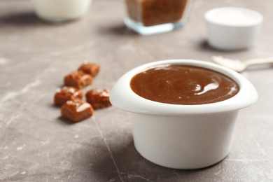 Photo of Bowl with tasty caramel sauce on grey table. Space for text