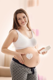 Pregnant woman with heart painted on her belly against blurred background