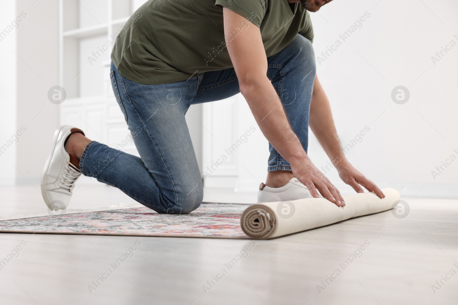 Photo of Man unrolling carpet with beautiful pattern on floor in room, closeup