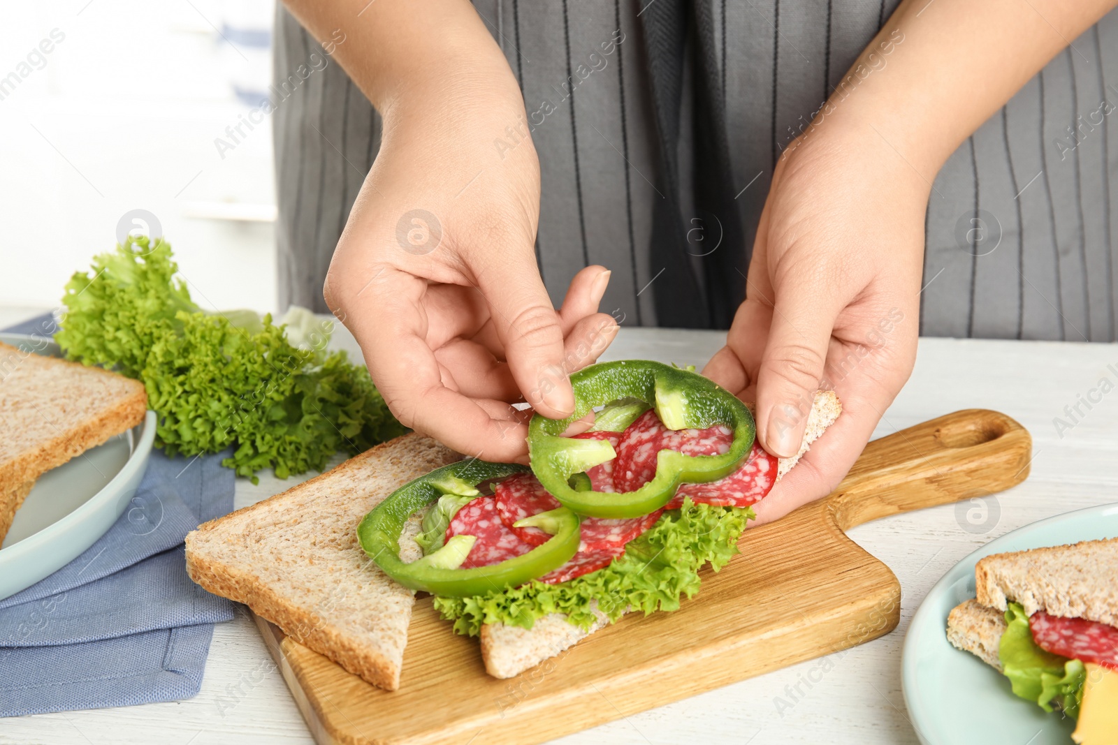 Photo of Woman making sandwich with green bell pepper and sausage at white table, closeup