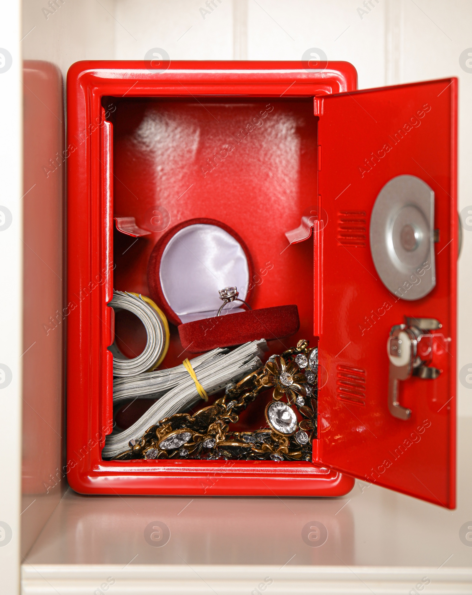 Open red steel safe with money and jewelry on shelf Photo of Open red steel safe with money and jewelry on shelf